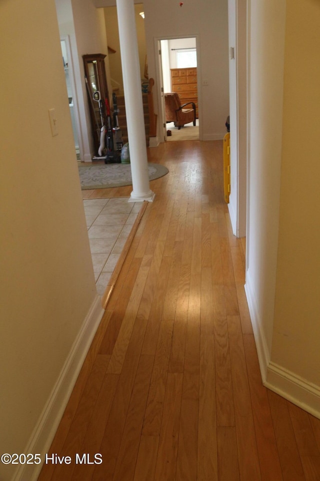 hallway with ornate columns, light wood-style floors, and baseboards