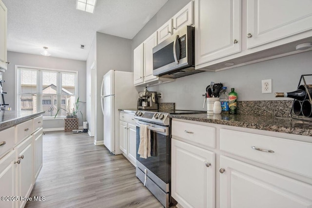 301 Softwood Ct, Jacksonville, NC 28540 - kitchen with light wood-style flooring, a textured ceiling, white cabinetry, dark stone countertops, and stainless steel appliances