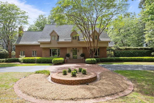 cape cod house with brick siding, a shingled roof, a chimney, and a front lawn