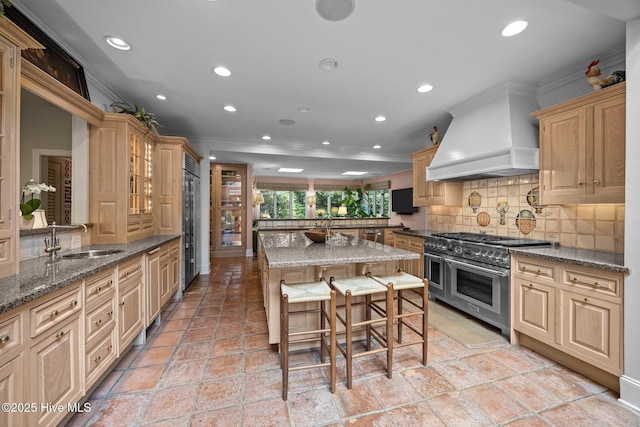 kitchen with crown molding, high end appliances, recessed lighting, custom range hood, and a sink