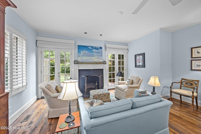 living area featuring ceiling fan, a fireplace, wood finished floors, baseboards, and ornamental molding