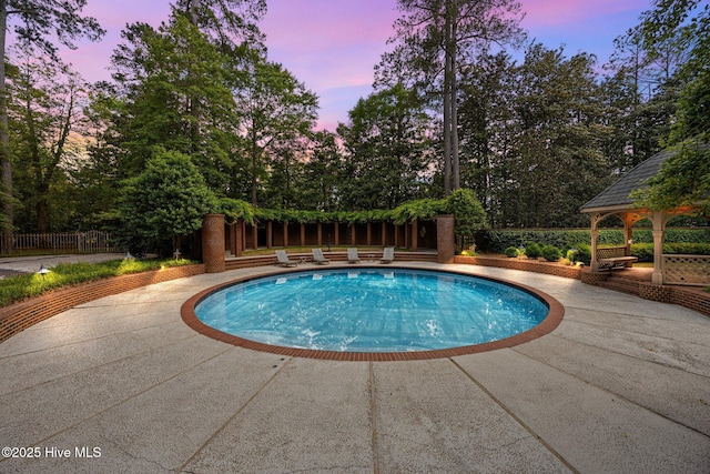 pool at dusk featuring a gazebo, a patio area, an outdoor pool, and fence
