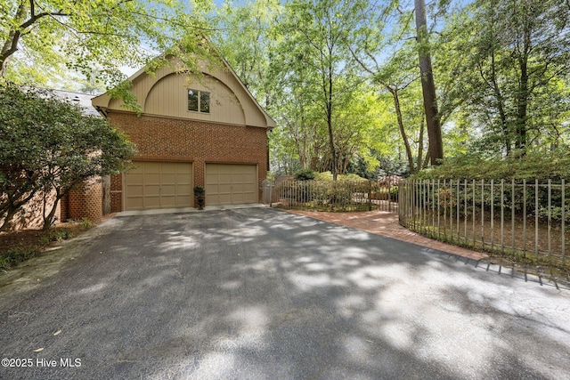 view of property exterior with an attached garage, aphalt driveway, fence, and brick siding