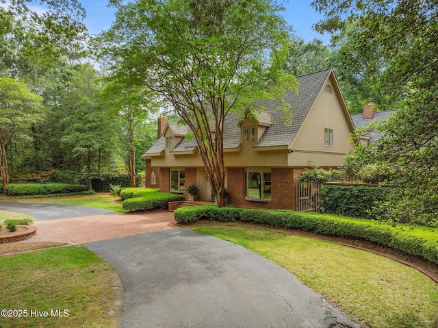view of front of house with brick siding, driveway, a chimney, and a front yard