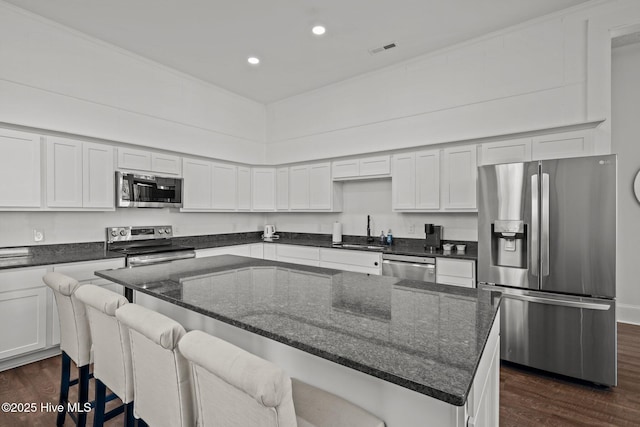 kitchen featuring visible vents, a sink, stainless steel appliances, dark wood-type flooring, and a kitchen island