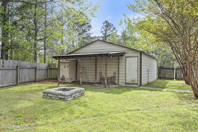 view of outdoor structure featuring an outbuilding, a fenced backyard, and an outdoor fire pit