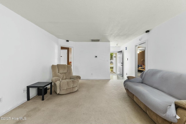 living area with visible vents, light colored carpet, and a textured ceiling
