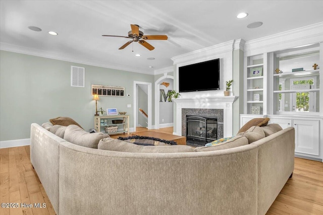 living area with ornamental molding, a fireplace, light wood-style flooring, visible vents, and ceiling fan