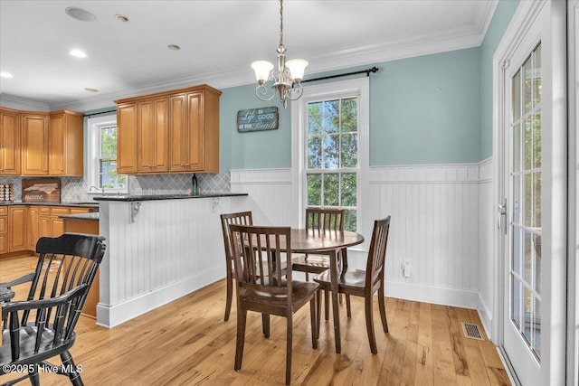 dining space with light wood finished floors, a notable chandelier, ornamental molding, and a wainscoted wall
