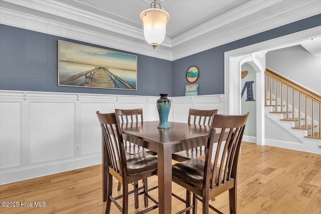 dining room featuring a decorative wall, light wood-style flooring, crown molding, and wainscoting