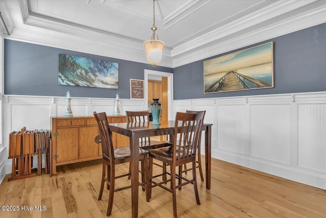 dining room with a decorative wall, ornamental molding, hardwood / wood-style floors, wainscoting, and a raised ceiling