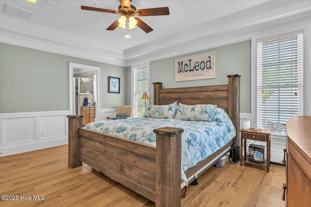 bedroom featuring a decorative wall, light wood-style flooring, ornamental molding, visible vents, and a wainscoted wall