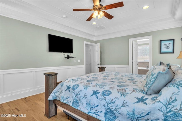 bedroom with ornamental molding, light wood-type flooring, a tray ceiling, and wainscoting
