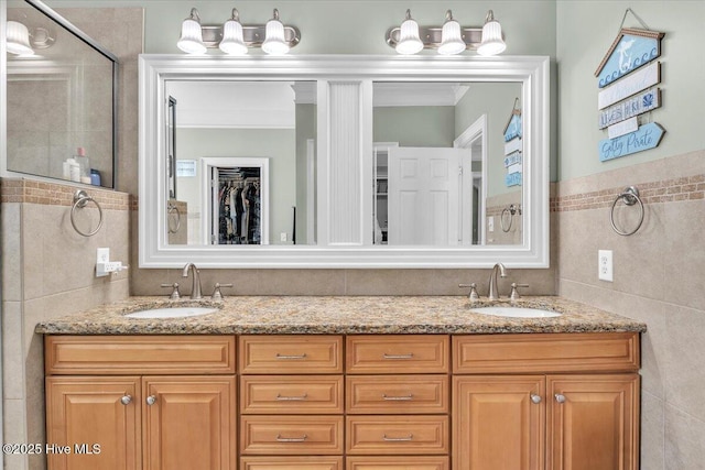 full bathroom with a sink, tile walls, a shower stall, and double vanity