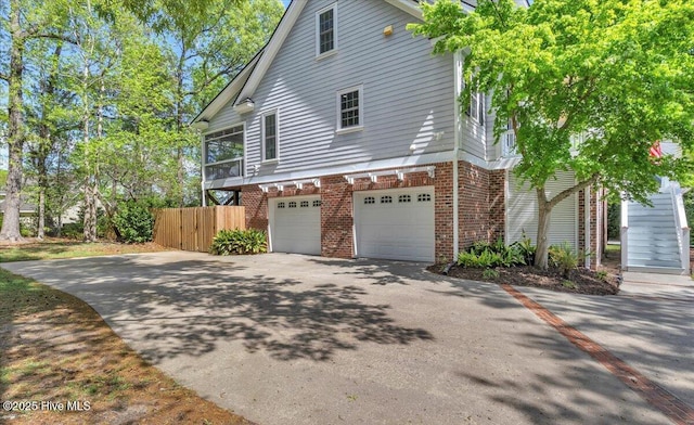 view of property exterior featuring aphalt driveway, a garage, fence, and brick siding