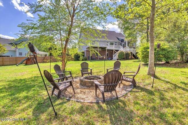 view of yard featuring a wooden deck, an outdoor fire pit, a playground, fence, and stairs