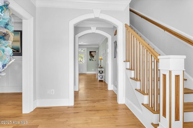 corridor featuring arched walkways, stairway, light wood-type flooring, and ornamental molding