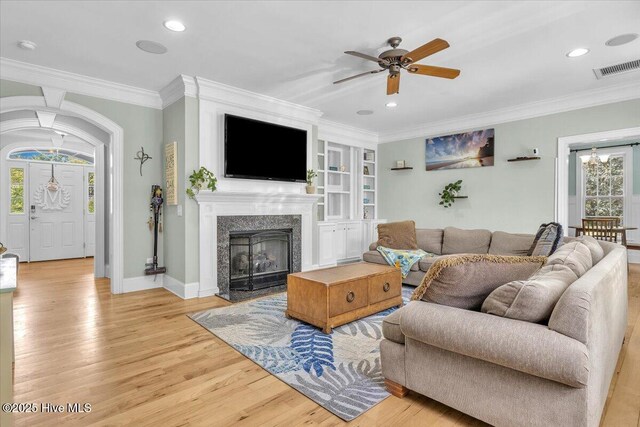 living area featuring light wood-style flooring, a ceiling fan, ornamental molding, and visible vents