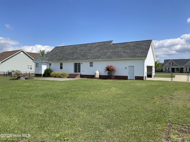 back of property with concrete driveway, roof with shingles, and a lawn