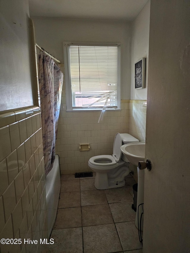 bathroom featuring toilet, tile patterned floors, tile walls, and a wainscoted wall