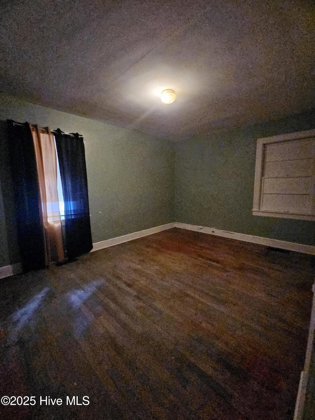 unfurnished room with dark wood-type flooring and baseboards
