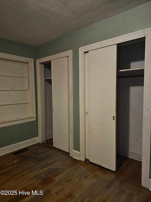 unfurnished bedroom with visible vents, multiple closets, wood finished floors, and baseboards