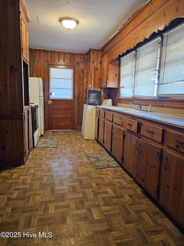kitchen featuring a sink, light countertops, freestanding refrigerator, wooden walls, and electric range