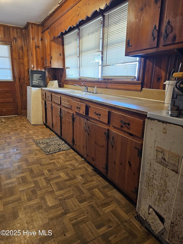kitchen featuring brown cabinetry, wooden walls, light countertops, and a sink