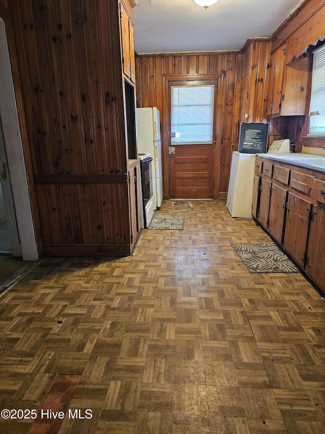 kitchen with freestanding refrigerator, washer / clothes dryer, wood walls, a sink, and light countertops