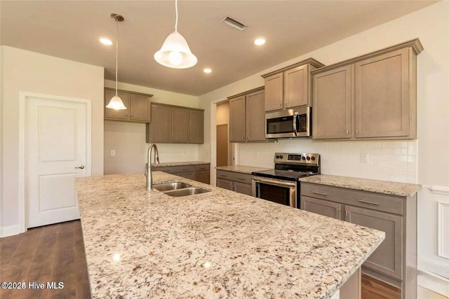 kitchen with light stone counters, a sink, stainless steel appliances, an island with sink, and backsplash