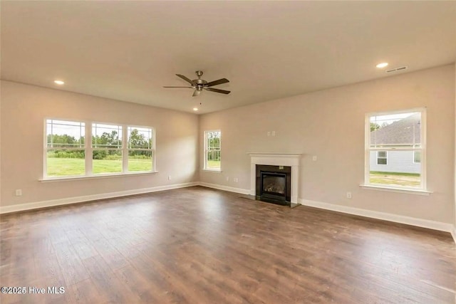 unfurnished living room featuring baseboards, a ceiling fan, dark wood-type flooring, and a glass covered fireplace