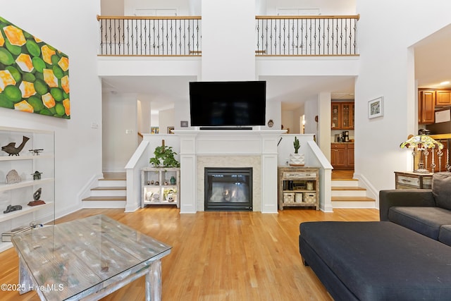living room with a towering ceiling, baseboards, stairway, light wood-style flooring, and built in shelves