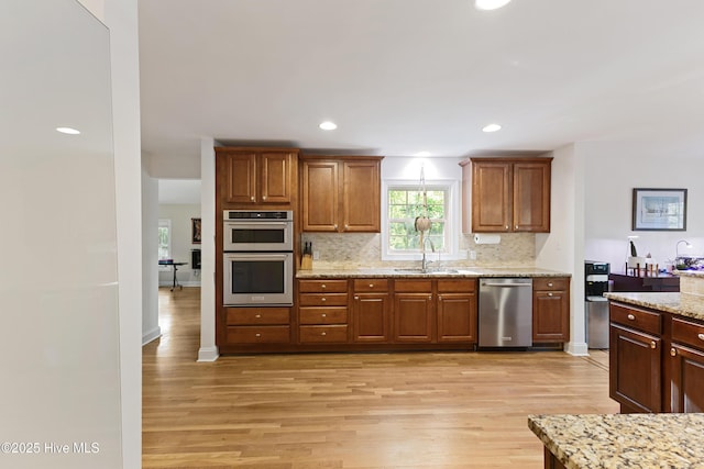 kitchen with light wood-style floors, light stone countertops, appliances with stainless steel finishes, a sink, and decorative backsplash