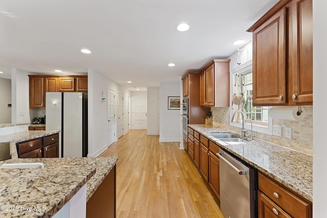 kitchen with light wood-type flooring, appliances with stainless steel finishes, decorative backsplash, and a sink