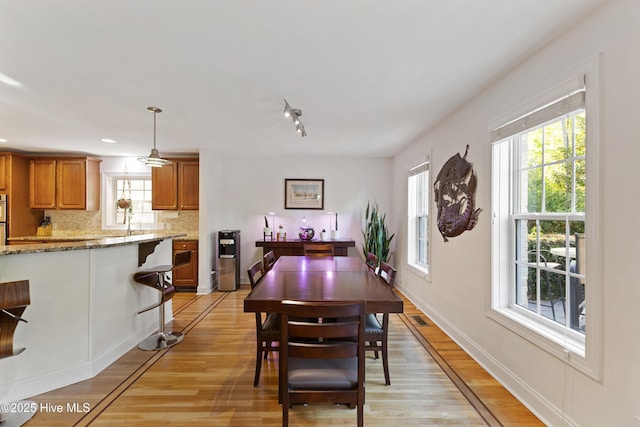 dining area with baseboards, light wood finished floors, and rail lighting
