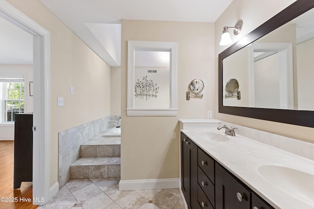 full bathroom with a sink, baseboards, double vanity, and a garden tub