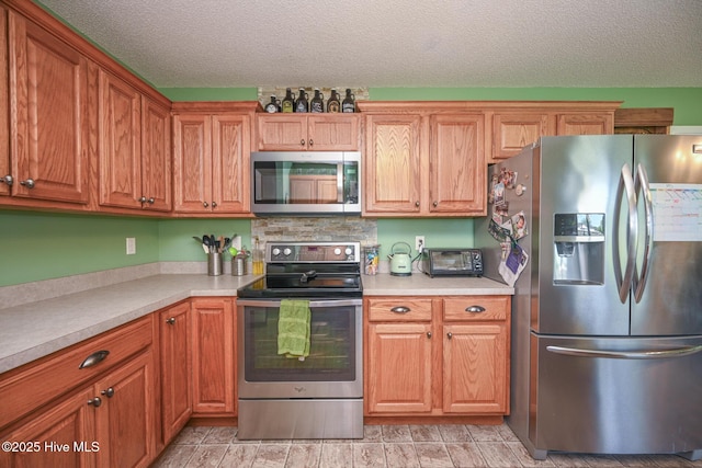 kitchen featuring a textured ceiling, brown cabinets, light countertops, and stainless steel appliances
