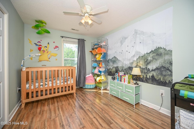 bedroom featuring baseboards, a textured ceiling, visible vents, a nursery area, and wood finished floors