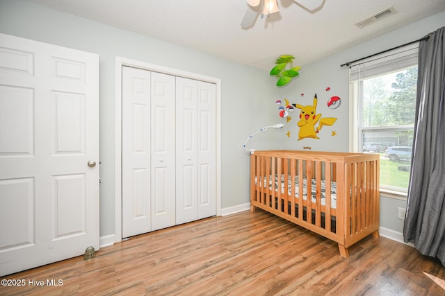 bedroom with visible vents, a closet, baseboards, a nursery area, and light wood-style flooring