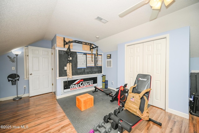 workout area with visible vents, baseboards, a textured ceiling, wood finished floors, and vaulted ceiling