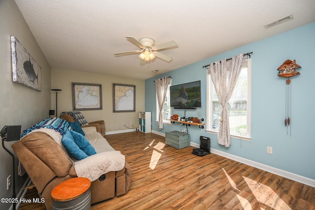 living area featuring ceiling fan, a textured ceiling, visible vents, wood finished floors, and baseboards