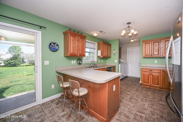 kitchen with a notable chandelier, a peninsula, washing machine and clothes dryer, stainless steel appliances, and a sink