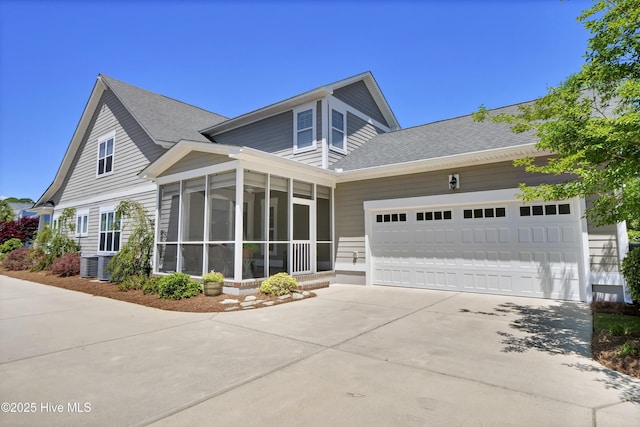 view of front of property featuring driveway, central AC unit, a sunroom, an attached garage, and a shingled roof