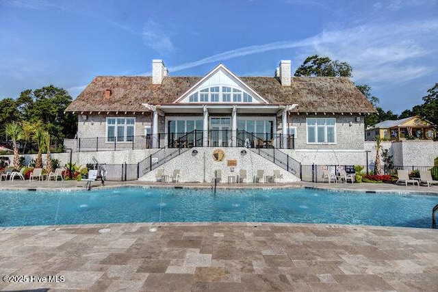 back of property featuring a chimney, a community pool, stairway, fence, and a patio