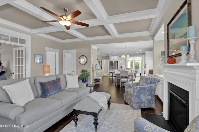 living room featuring crown molding, dark wood-style flooring, a fireplace, coffered ceiling, and ceiling fan with notable chandelier