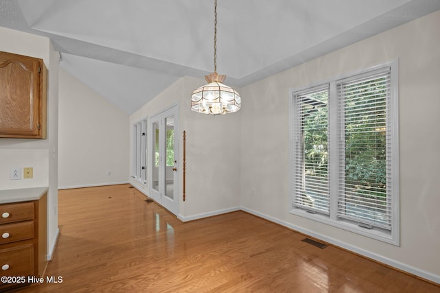 unfurnished dining area featuring baseboards, vaulted ceiling, light wood-type flooring, an inviting chandelier, and visible vents