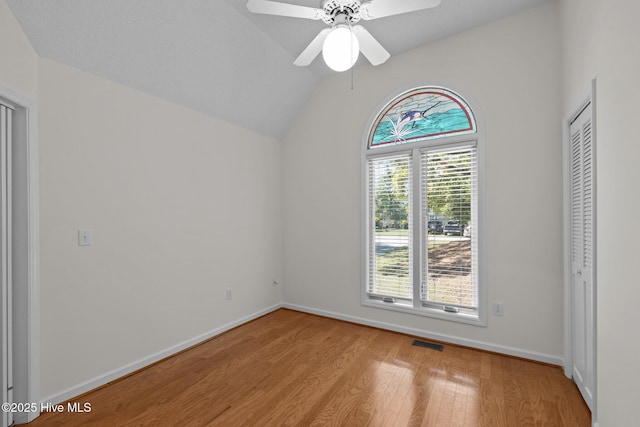 spare room featuring baseboards, vaulted ceiling, light wood-style flooring, a ceiling fan, and visible vents