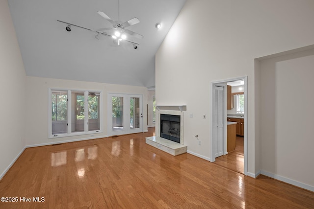 unfurnished living room featuring high vaulted ceiling, ceiling fan, light wood-style flooring, a fireplace with raised hearth, and baseboards