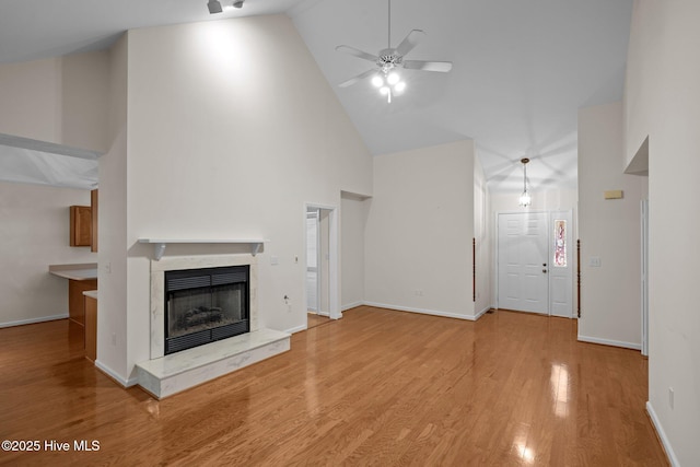 unfurnished living room featuring high vaulted ceiling, a ceiling fan, wood finished floors, a premium fireplace, and baseboards