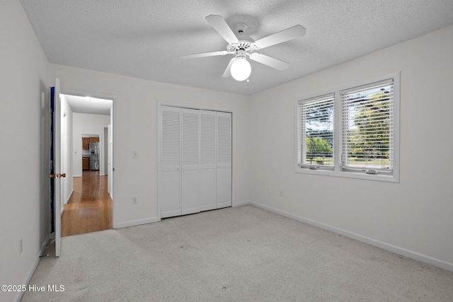 unfurnished bedroom featuring a closet, baseboards, light colored carpet, and a textured ceiling
